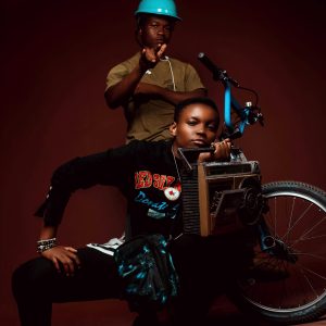 Two Young Men In A Studio With Bike And Boom Box Showcasing Trendy Fashion.