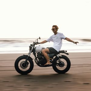 Young Man Enjoying A Carefree Motorcycle Ride On A Bali Beach, Showcasing Leisure And Adventure.