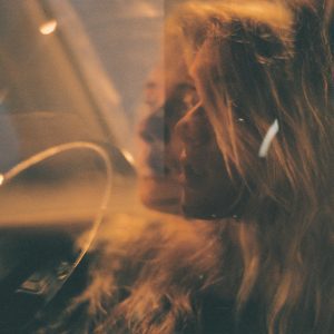 Blonde Woman In Car With Artistic Reflection At Night, Dimly Lit Setting.