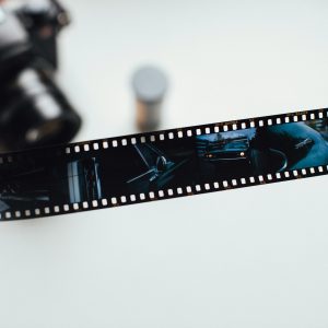 Close Up Of A Hand Holding A Vintage Film Strip With A Blurred Camera In The Background, Evoking Nostalgia.