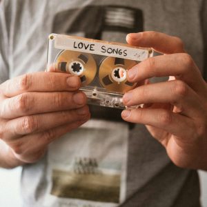 Close Up Of Hands Holding Retro Cassette Labeled 'Love Songs', Capturing Nostalgic Vibes.