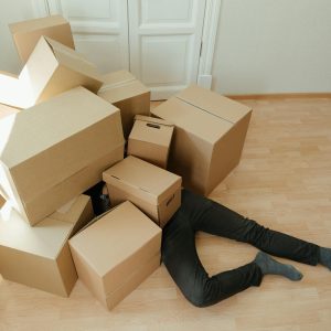 A Person Overwhelmed By Cardboard Boxes During A Home Move, Symbolizing Stress And Relocation.