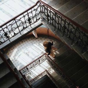 A Woman In A Vintage Setting Descends A Patterned Staircase, Captured From Above.