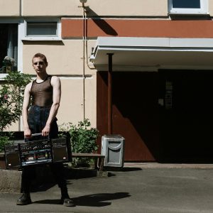 A Young Man Holding A Vintage Boombox In Front Of A Building Facade.