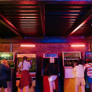 Group Of Teenagers Playing Retro Arcade Games Together. Colorful Indoor Scene.