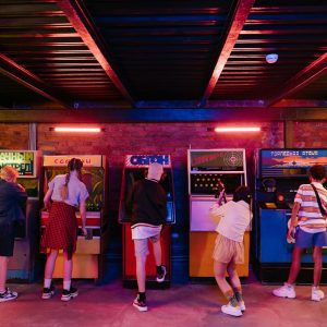 Group Of Teenagers Playing Various Retro Arcade Games, Enjoying A Nostalgic Gaming Experience.