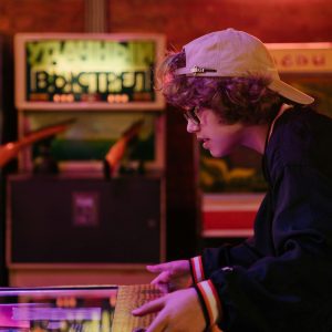 Teenager Enjoying A Game Of Pinball In A Vibrant, Retro Themed Arcade.