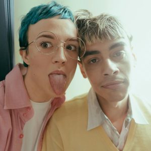 Two Trendy Teenagers In A Photobooth, Showing Playful Expressions With Colorful Styles.