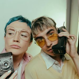 Two Stylish Teenagers Posing With Retro Accessories In A Photobooth, Capturing A Vintage Vibe.
