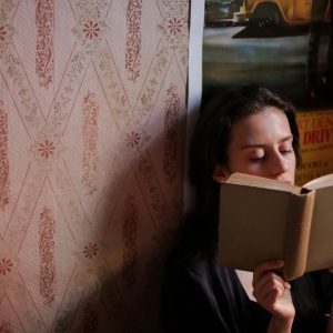 A Young Woman Deeply Engrossed In A Book, Surrounded By Vintage Wallpaper Indoors.