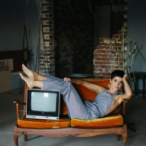 Stylish Woman Posing On Vintage Sofa With An Old TV In A Rustic Setting.