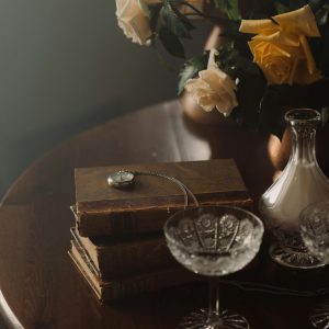 A Serene Still Life Featuring Vintage Books, A Pocket Watch, And A Bouquet Of Roses On A Wooden Table.