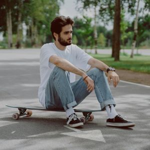 Casual Young Man Sitting On A Skateboard In A Park, Exuding Urban And Relaxed Vibes.