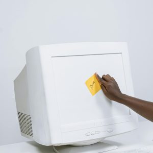 Vintage CRT Monitor In A Minimalist Workspace With A Hand Placing A Note On The Screen.