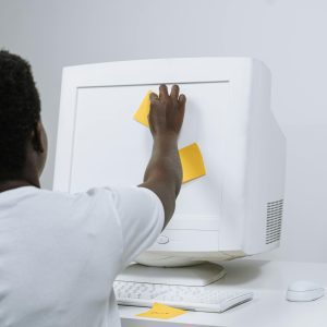 A Man Places Sticky Notes On An Old CRT Computer, Capturing Retro Workplace Vibes.