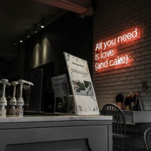 Intimate Cafe Setting With A Neon Sign Reading 'All You Need Is Love (and Cake)'