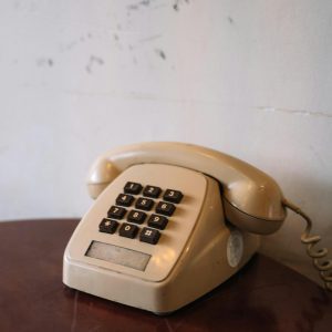 A Classic Beige Corded Rotary Telephone Placed On A Wooden Table, Evoking A Retro Feel.