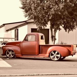 Classic Red Pickup Truck Parked In An Urban Area With Buildings And Trees In The Background.