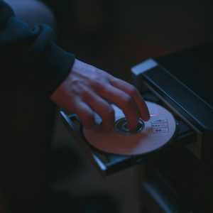 A Hand Inserting A CD Into A Computer Drive, Highlighting Cyber Security Themes.