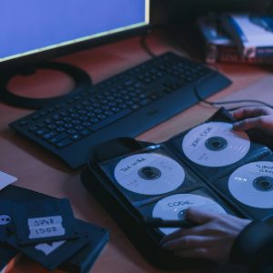 A Close Up Of CDs And Disks On A Desk, Featuring Hands In A Tech Environment.