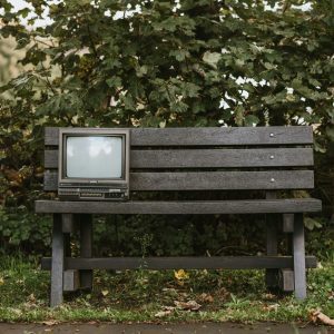 Retro Television Set On An Outdoor Bench Surrounded By Lush Greenery, Evoking Nostalgia.