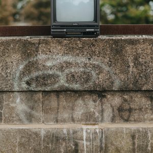 Black Old Fashioned Placed On Shabby Stone Fencing With Graffiti In City On Street With Green Trees On Blurred Background