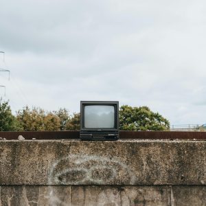 A Retro TV Set Sits On A Graffitied Concrete Wall With Trees And Power Lines In The Background.