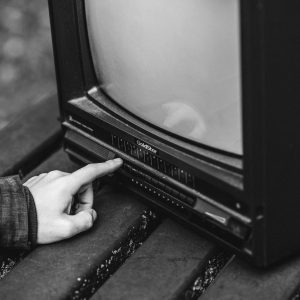 Black And White Of Unrecognizable Male Pressing Buttons On Old Fashioned Television Placed On Wooden Table In Nature On Blurred Background