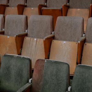 A Weathered And Dusty Row Of Wooden Seats In An Empty Theater, Showcasing Industrial Decay.