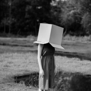 Black And White Photo Of A Woman Outdoors In Nature, Head Hidden In A Box.