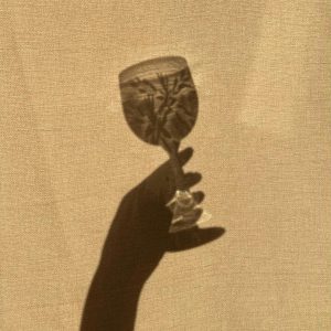 Shadow Of A Hand Holding A Vintage Glass Against A Textured Background In Sepia Tones.