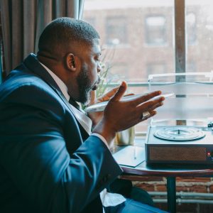 African American Man In A Suit Engaging With A Turntable, Indoors.