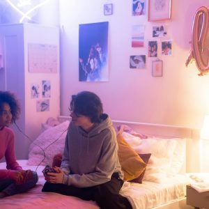 Two Teenagers Sharing A Music Player In A Cozy Bedroom With Warm Lighting.