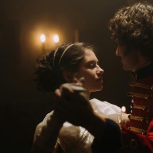 A Couple Dressed In Vintage Attire Elegantly Dances Indoors Under Soft Candlelight.