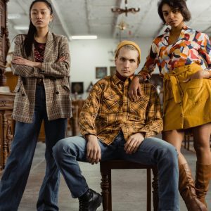 Three Models In Stylish Outfits Pose During A Fashion Photoshoot In A Vintage Store Setting.
