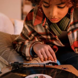 A Young Woman Listens To Music On A Retro Turntable With Headphones Indoors.