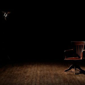 A Vintage Wooden Chair Is Spotlighted In A Dark Studio Setting, Casting Shadows.