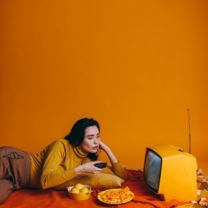 Woman In Yellow Outfit Watching Vintage TV With Snacks In Yellow Themed Room.