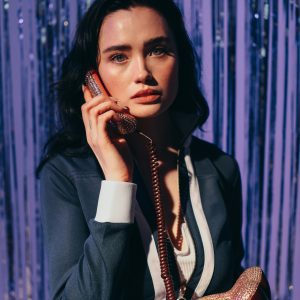 Stylish Woman In A Retro Outfit Talking On A Glitter Phone Indoors With A Disco Vibe.