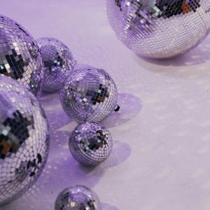 A Collection Of Disco Balls Casting Reflections On A Purple Lit Floor, Creating A Vibrant Atmosphere.