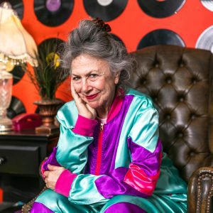 Stylish Elderly Woman In Colorful Outfit Posing With Vinyl Records In A Retro Themed Room.