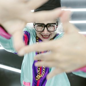 Senior Woman Posing Playfully In Vibrant Retro Outfit With Fun Accessories.