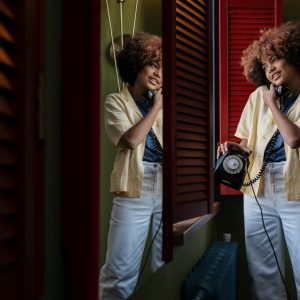 A Cheerful Young Woman With Afro Hair Using A Vintage Rotary Phone, Reflecting Joy And Nostalgia.