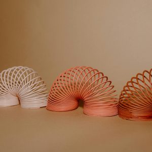 A Vibrant Row Of Slinkies Displaying Gradient Rainbow Colors On A Neutral Backdrop.