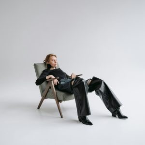 Stylish Woman In Black Leather Outfit Reclines In A Minimalist Studio With Open Space.