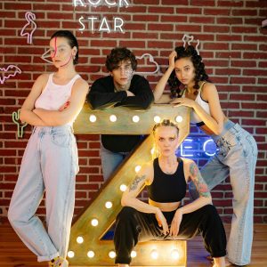 Fashionable Group Of Gen Z Posing With Neon Lights And Art Makeup Against A Brick Wall.