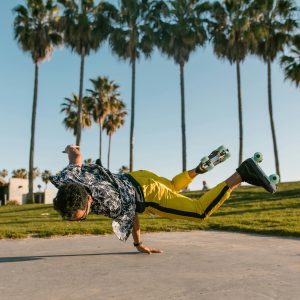 Young Adult Roller Skater Performs A Trick Under Palm Trees In A Sunny Outdoor Park.