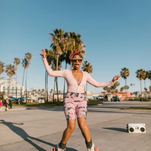 Stylish Woman Roller Skating At A Beachside Park With Palm Trees Under A Clear Blue Sky.