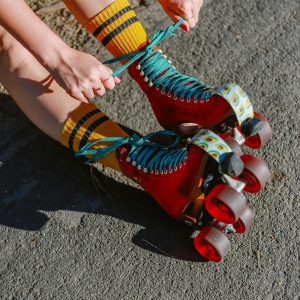 Close Up Of A Person Tying Red Roller Skates Outdoors, Capturing Vibrant Colors.