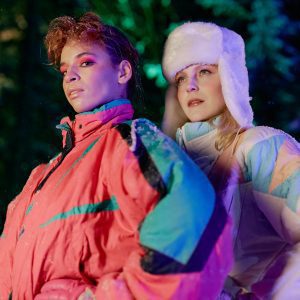 Two Fashionable Women Posing In Colorful Winter Jackets During A Nighttime Forest Photoshoot.